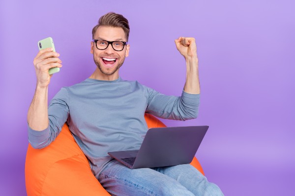 homme souriant en tenant son téléphone et son ordinateur 